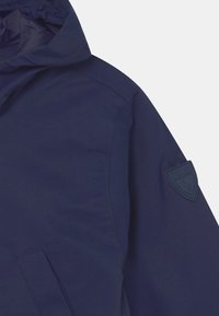 Marinblå hoodie-jacka med en mjuk textur, som har en subtil logopatch på ärmen och en sidofickdetalj.