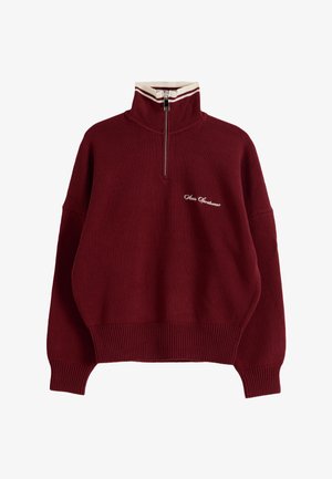 Maglione bordeaux in maglia con colletto alto a righe bianche, zip frontale, polsini e orlo a coste, e piccolo logo script bianco sul petto.