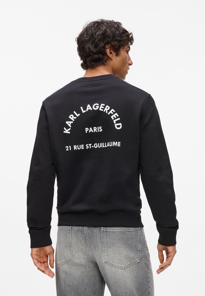 Sudadera negra con cuello redondo, puños y dobladillo de canalé. Presenta texto blanco en la espalda: "KARL LAGERFELD PARIS 21 RUE ST-GUILLAUME."