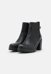 Czarne skórzane botki za kostkę z masywnym obcasem, zaokrąglonym noskiem, elastycznymi panelami po bokach oraz ozdobną złotą klamrą. Podeszwa o fakturze zwiększającej przyczepność.