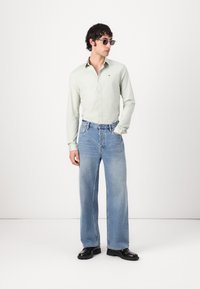 Cămașă butonată verde deschis, blugi lejerați albastru deschis și pantofi negri. Ochelarii de soare adaugă o notă modernă. O ținută simplă și casual.