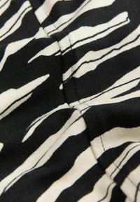 Tessuto nero e beige con motivo a strisce zebrate e cuciture visibili lungo le giunture.