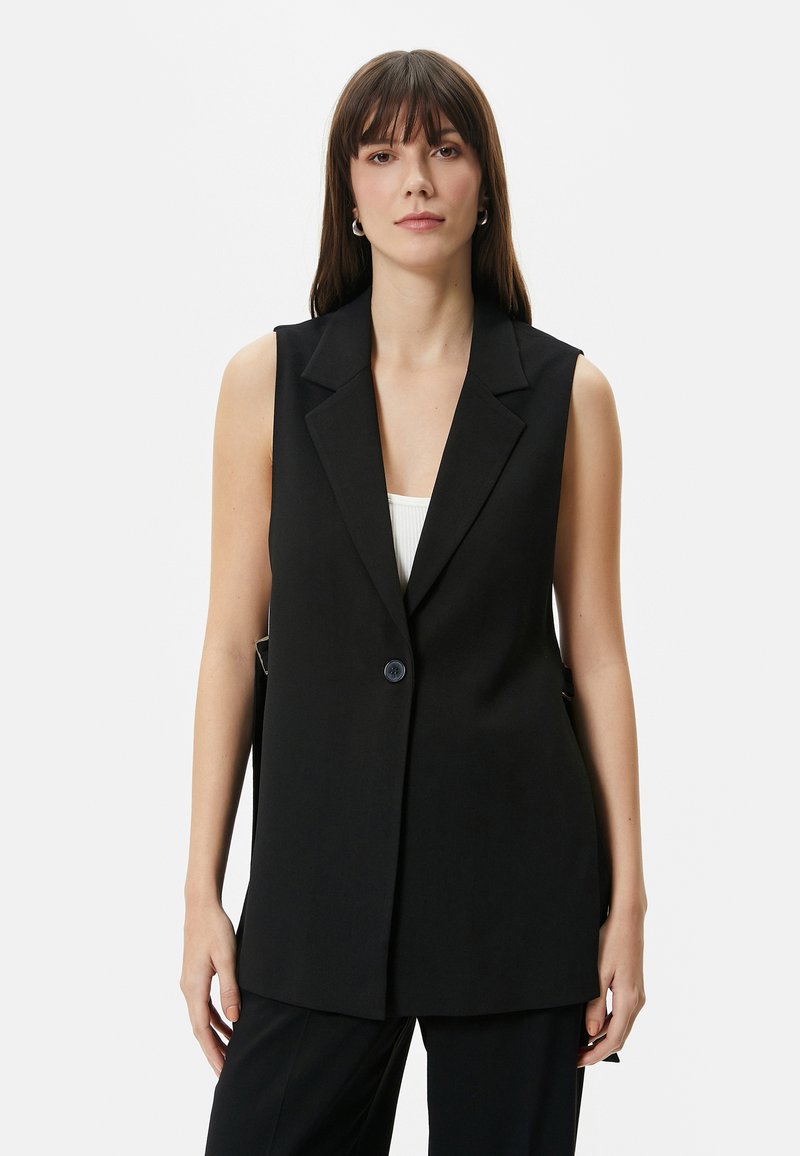 Schwarze ärmellose Blazerjacke mit Reverskragen, einem Knopfverschluss und seitlichen Taschen. Hergestellt aus glattem Stoff mit taillierter Passform.