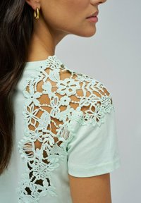 Camiseta verde menta con detalles de encaje floral en los hombros, con un patrón texturizado y mangas cortas.