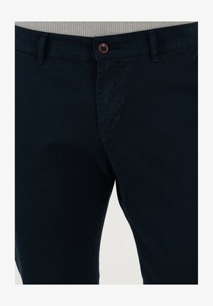 Navy blue chinos made of smooth cotton fabric. Features a button closure with a contrasting red button, angled front pockets, and belt loops.