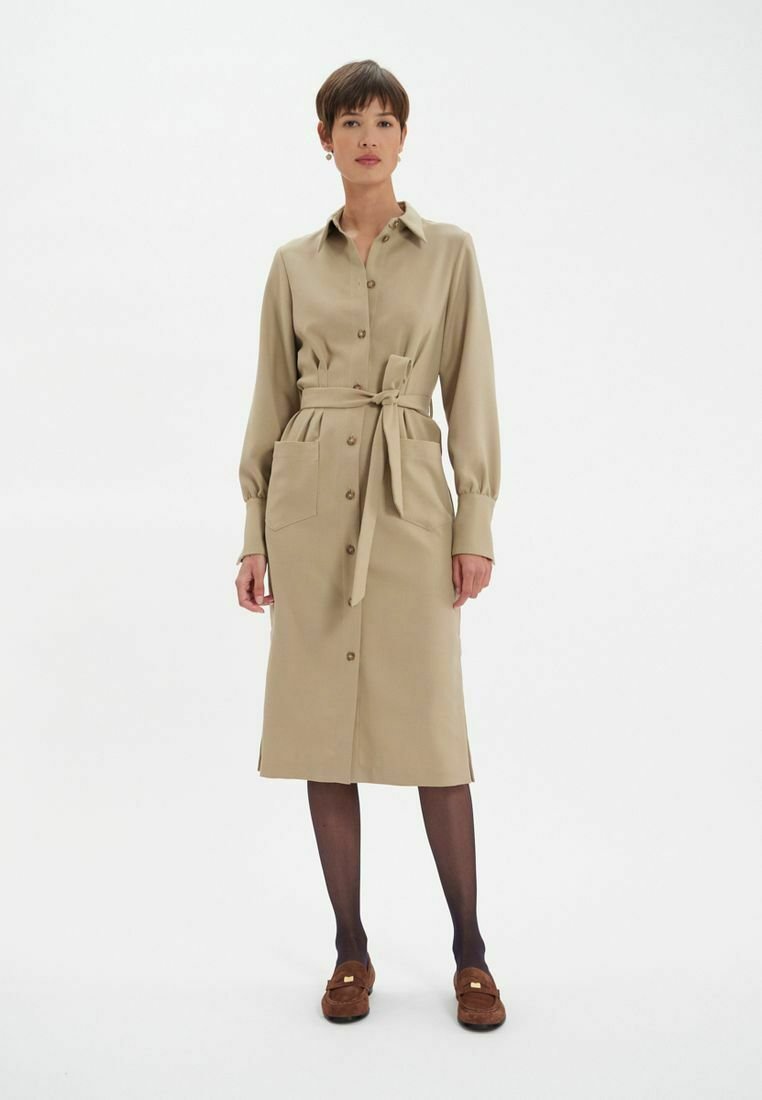 Robe beige à boutons avec des manches longues, taille ceinturée, deux poches avant, fabriquée dans un tissu doux, tombe sous le genou.