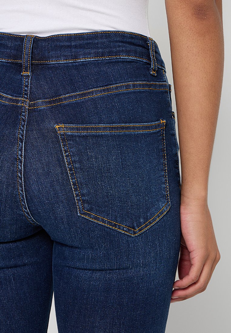 Dunkelblaue Jeans aus Denim haben eine taillierte Passform, auffällige gelbe Nähte und zwei klassische Gesäßtaschen.