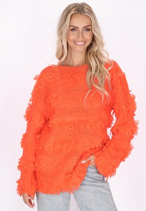 Maglione lavorato a maglia arancione con un design a frange testurizzato, caratterizzato da maniche larghe e una vestibilità comoda, abbinato a jeans in denim chiaro.