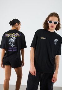Black cotton graphic t-shirts with oversized fit. Front has a white flower print, back features colorful text and design elements.