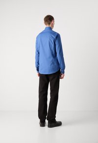 Camicia blu a maniche lunghe con colletto punto, polsini con bottone e orlo curvo, abbinata a pantaloni neri e scarpe nere.
