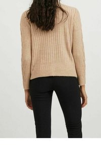 Maglione beige a coste con maniche lunghe e dettagli texturizzati, abbinato a pantaloni neri attillati. La vista mostra la parte posteriore dell'outfit.
