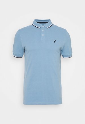 Polo bleu clair à manches courtes avec liseré blanc et noir sur le col et les manches, deux boutons et petit logo noir brodé sur la poitrine.