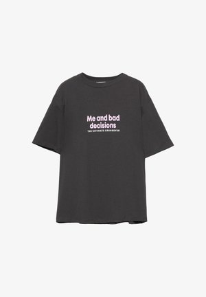 Harmaa löysä puuvillapaita, jossa on vaaleanpunaista tekstiä "Minä ja huonot päätökset" ja "ULTIMAATTIYHDISTELMÄ." Lyhyet hihat, pyöreä kaula-aukko.