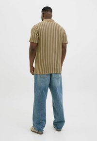 Brun och krämrandig kortärmad skjorta med krage, ihop med ljusblå, löst sittande jeans och beigefärgade slip-on skor.