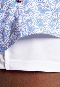 Light blue floral-patterned fabric drapes over a white, smooth-textured layer, highlighting distinct shapes and clean stitching at the hem.