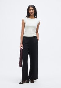 Ελαφρύ κρεμ, εφαρμοστό αμάνικο τοπ σε συνδυασμό με ψηλόμεσα, φαρδιά μαύρα παντελόνια. Το μοντέλο κρατάει μια μπορντό τσάντα και φοράει σκούρα παπούτσια.