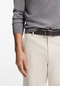 Γκρι πουλόβερ με ριμπ μανσέτες, συνδυασμένο με ανοιχτό μπεζ παντελόνι και σκούρο πλεκτό δερμάτινο ζωνάρι με ασημένια πόρπη. Χέρι στηρίζεται πάνω στο παντελόνι.