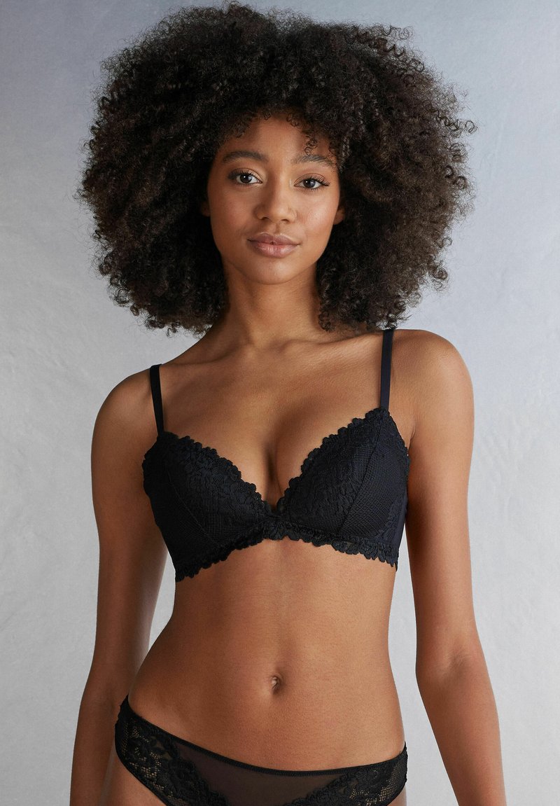 Svart spetsbehå med djup V-ringning, scallopade kanter och justerbara band. Materialet har en mjuk textur med blommönster.