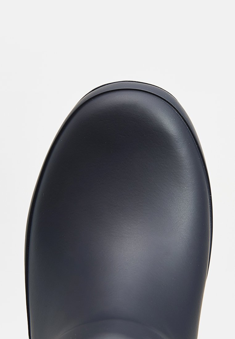 Bota de goma negra con puntera redondeada, textura suave y diseño sin costuras. La parte superior es brillante con un perfil bajo.