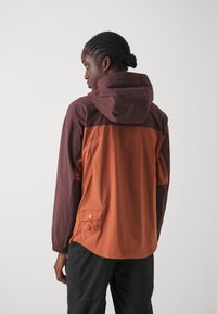 Vindjakke med hette, med en fargeblokk-design i brent oransje og mørkebrunt, teksturert stoff og en sidelomme med knapp.