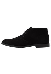 Bottines en daim noir avec un bout arrondi, un design minimaliste et des lacets gris, associées à une semelle en caoutchouc noir uni.