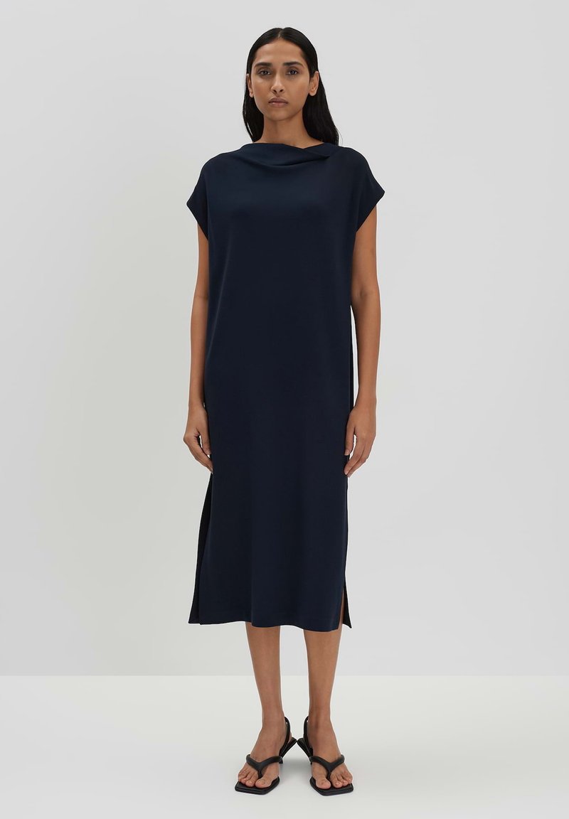 Marineblaue Midikleid mit kurzen Ärmeln, schalenförmigem Ausschnitt, Seitenschlitzen und einem glatten, fließenden Stoff. Getragen mit flachen schwarzen Sandalen.