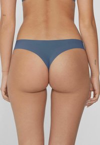 Bañador inferior azul con una textura suave, cobertura mínima y un diseño de tiro bajo. Presenta un acabado sin costuras y aberturas de pierna curvadas.