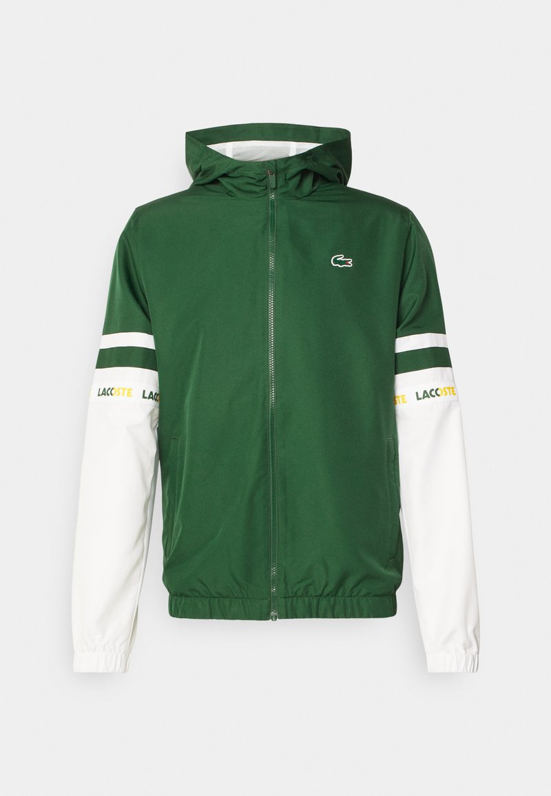 Grüne und weiße Zip-Jacke mit Kapuze. Merkmale das Lacoste-Logo, gestreifte Akzente an den Ärmeln und elastische Bündchen. Glatte Stoffstruktur.