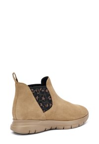 Botas de tobillo de ante color marrón con inserciones elásticas laterales negras que presentan un patrón. Punta redondeada y una suela de goma flexible con un acabado texturizado.