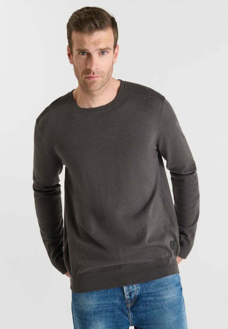 Grå stickad tröja med rund halsringning, ribbade axeldetaljer och långa ärmar, bärs med blå denimjeans. Mjuk textur och avslappnad passform.