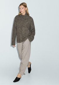 Oversized, gestructureerde donkere gebreide trui met een hoge kraag, gecombineerd met lichtgrijze wijde broek en zwarte muilen. Eenvoudig, neutraal kleurenpalet.