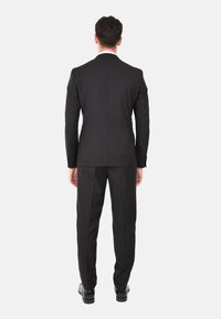 Completo nero con una vestibilità su misura, caratterizzato da una texture liscia, design monopetto e pantaloni coordinati. La vista posteriore mette in mostra linee pulite e dettagli sottili.