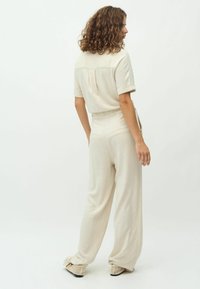 Conjunto de dos piezas en un tono beige claro, que incluye una blusa de manga corta y pantalones sueltos con corte relajado y bolsillos traseros. Tela texturizada.