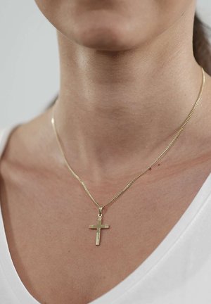 Goldfarbene Kreuzkette mit strukturiertem Design, aufgehängt an einer dünnen Kette, über einem weißen V-Ausschnitt-Oberteil getragen.