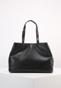 Černá kožená taška přes rameno s dvojitými ramenními popruhy, jemnou texturou a prostorným designem bez víka. Mírně zaoblené rohy a žádné viditelné kování.