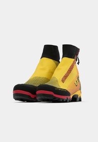 Botas impermeables de corte alto, amarillas con acentos negros, superficie texturizada y suelas de gran profundidad. Cuenta con un zipper lateral y un logo de marca.