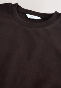 Sweatshirt en coton marron foncé avec un col rond côtelé. Présente une texture subtile et des coutures visibles. Étiquette de la marque visible à l'intérieur du col.