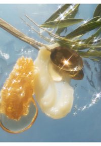 Gyldent honungsflarn och tjock vit kräm är placerade bredvid en metallsked mot en blå bakgrund, framhävt av skimrande ljus.