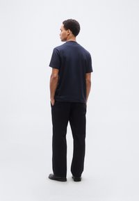 Μπλε ναυτικό polo με κοντά μανίκια και ίσια γραμμή, συνδυασμένο με μαύρο παντελόνι. Μινιμαλιστικός σχεδιασμός, λεία υφή και χωρίς εμφανή μοτίβα ή διακοσμητικά στοιχεία.