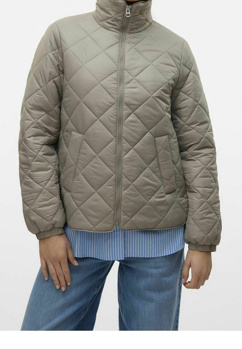 Virkattu, lysgrå jakke med høy krage, frontglidelås og ribbede mansjetter. Båret over en blåstripet skjorte og sammen med blå jeans.