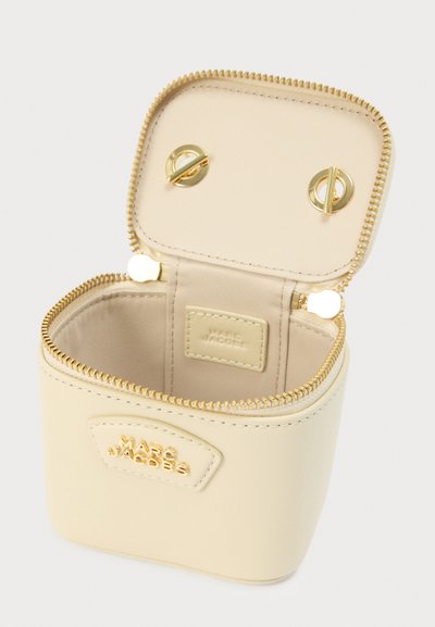 Μπεζ δερμάτινη καλλυντική θήκη με στρογγυλεμένο σχήμα, κλείσιμο με χρυσό φερμουάρ και επώνυμη ετικέτα στο μπροστινό μέρος. Το εσωτερικό επενδύεται με ύφασμα σε αντίστοιχο χρώμα.