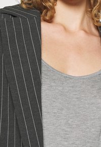 Grijze pinstriped blazer met gestructureerde schouders, gecombineerd met een lichtgrijze, mouwloze, ronde hals tanktop. Zachte texturen en casual lagen.