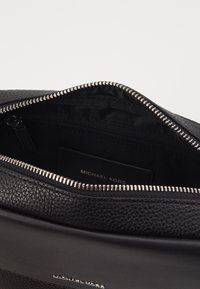 Borsa in pelle nera con esterno testurizzato, chiusura superiore con zip e rivestimento interno. Presenta hardware argentato e un'etichetta del brand all'interno.
