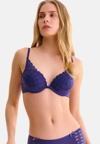 Soutien-gorge en dentelle violette avec un motif matelassé, des bords festonnés et des bretelles ajustables. Tissu doux avec une conception structurée pour un bon maintien.