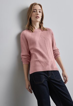 Pull en tricot rose pâle avec texture côtelée, présentant un motif diagonal et un col rond. Associé à un jean en denim bleu foncé.