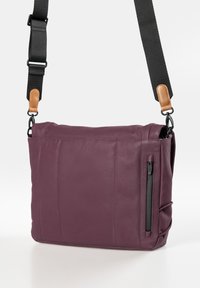 Borse a tracolla viola con cintura nera regolabile, dettagli in pelle marrone e tasca laterale con zip verticale.