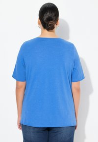 Camiseta azul de manga corta con cuello redondeado, confeccionada en una tela suave, que presenta un corte holgado y un dobladillo ligeramente curvado en la parte posterior.