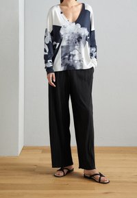 Pull à manches longues en v blanc et marine avec imprimé floral, associé à un pantalon large plissé noir et des sandales noires.