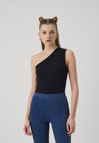 En-ermet svart ribbet bodysuit kombinert med lyseblå glitrende høytlivs bukser. Modellen står mot en enkel hvit bakgrunn.