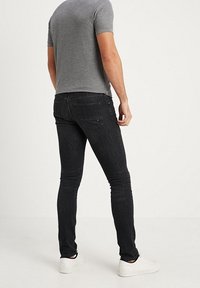 Grå t-shirt, svarta slim-fit jeans med bakfickor, och vita sneakers. Tyget verkar slätt med en lätt stretch.